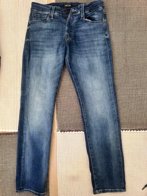 Blå slim fit jeans från Jack&jones - Snygga blå slim fit jeans från Jack&jones med klassisk femficksmodell och lätt slitna detaljer. Jeansen har normal midja och raka ben, tillverkade i mjuk denim med stretch för extra komfort. Perfekta till en avslappnad streetstyle-look.