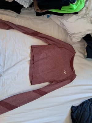 Vinröd långärmad träningströja - Vinröd långärmad träningströja med diskret mönster och tumhål i ärmsluten. Tröjan har rund halsringning och är tillverkad i ett stretchigt funktionsmaterial som andas. Perfekt för aktiva dagar eller som lager under jackan.