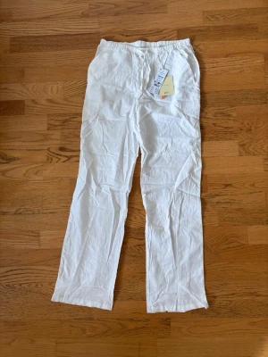 Vita linnebyxor med snören - Säljer ett par vita linnebyxor med rak passform. Byxorna är tillverkade i lätt och luftigt linnetyg, perfekta för en avslappnad och stilren look. Passar dig som gillar enkel och fräsch stil. I storlek 158/164 men passar mig som har XS/S