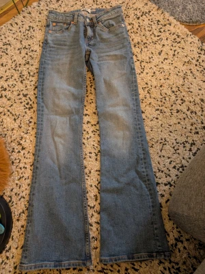 Blå bootcut jeans med fem fickor xxs - Säljer ett par klassiska blå bootcut jeans i denim med fem fickor och orangea sömmar. Jeansen har normalhög midja och utsvängda ben. Perfekta för dig som gillar retrostil och vill ha ett par bekväma jeans i tidlös modell.