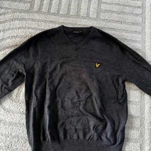 Mörkgrå V-ringad tröja Lyle & Scott - Mörkgrå V-ringad tröja från Lyle & Scott med klassisk gul logga på bröstet. Priset går alltid att diskutera!💕