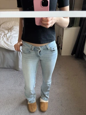 Ljusblå bootcut jeans låg midja - Säljer ett par ljusblå bootcut jeans med låg midja och klassiska fem fickor. Jeansen har en snygg tvätt och är tillverkade i stretchigt denimtyg för skön passform. Perfekta till en avslappnad look och passar till det mesta.