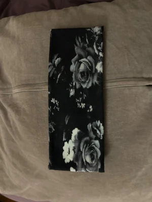 Svart hårband med vita rosor - Snygg svart hårband med stora vita rosor och blommönster. Tunn och mjuk, perfekt att slänga över axlarna för en cool touch till din outfit. Passar lika bra till jackan som till en enkel topp. Blommönstret ger en romantisk vibe.
