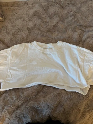 Vit croppad t-shirt PrettyLittleThing - Säljer en vit croppad t-shirt från PrettyLittleThing i 100% bomull. T-shirten har korta ärmar, rund halsringning och en loose passform. Perfekt till jeans eller shorts för en avslappnad look.