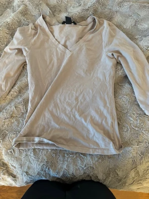 Beige v-ringad topp från H&M - Säljer en enkel och stilren beige topp från H&M i storlek XS. Toppen har v-ringning och trekvartsärm, tillverkad i mjuk bomull. Perfekt att matcha med jeans eller kjol för en clean look.