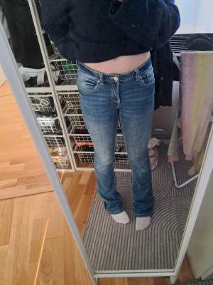 Blå bootcut jeans med kontrastsömmar - Säljer ett par blå bootcut jeans med snygga kontrastsömmar och klassiska fem fickor. Jeansen har normal midja och är i ett stretchigt denimtyg som sitter skönt. Bakfickorna har dekorativa sömmar som ger extra stil.