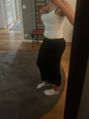 Svart långkjol i stretchigt material - Säljer en svart långkjol med figurnära passform. Kjolen är enkel och stilren utan synliga detaljer eller mönster, perfekt för dig som gillar en clean look. Materialet känns stretchigt och bekvämt, vilket gör den lätt att bära hela dagen.