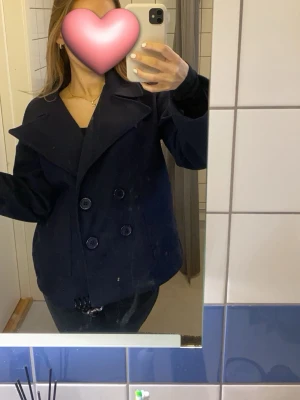 Mörkblå kappa från Design By Si - Stilren mörkblå kappa från Design By Si med dubbelknäppning och bred krage. Jackan har två framfickor och stora knappar framtill. Endast använd ett fåtal gånger!🩷Är i storlek XS/S