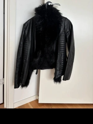 Svart skinnjacka med fuskpäls - Snygg svart skinnjacka från Bik Bok med mjuk fuskpäls på insidan och längs kragen. Jackan har quiltade detaljer på ärmarna och dragkedjor vid ärmsluten. Perfekt för dig som vill ha en edgy look med extra värme och stil.