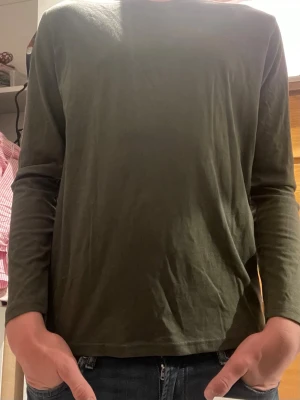 Olivgrön långärmad basic tröja - En enkel och stilren olivgrön långärmad tröja i mjukt bomullstyg. Tröjan har rund halsringning och rak passform, perfekt för en avslappnad look. Passar till jeans eller under en jacka. Storlek 170 men perfekt som XS