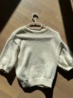 Krämvit stickad tröja med ballongärm - Säljer en krämvit stickad tröja med rund hals och ballongärmar i trekvartslängd. Tröjan har ribbstickade muddar vid hals, ärmslut och nederkant. Perfekt för dig som gillar en enkel men trendig look.