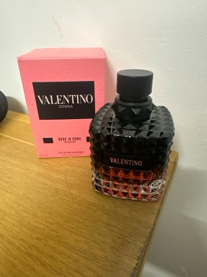 Valentino Donna Born In Roma Intense - Valentino Donna Born In Roma Intense är en lyxig parfym i en cool, svart och rosa glasflaska med nitar och elegant design. Flaskan har en fyrkantig form och svart kork. Förpackningen är rosa med svart etikett och text. Perfekt för dig som gillar exklusiva dofter och snygg design.