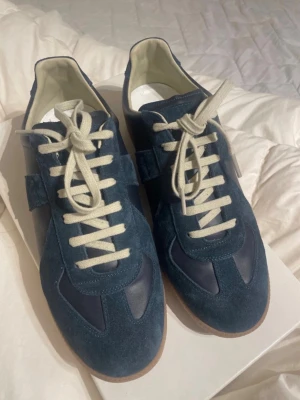  maison margiela - Snygga mörkblå sneakers med ovandel i mocka och detaljer i slätt läder. Skorna har vita snören och en klassisk gummisula. Perfekta för dig som gillar stilrena och tidlösa sneakers med en modern twist. Oanvänd i nyskick. Storlek 39. Får med lådan.😁
