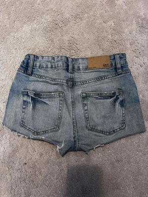 Blå jeansshorts från lager 157 - Säljer ett par blå jeansshorts från lager 157 i storlek 150, med råa, fransiga kanter och slitna detaljer framtill. 