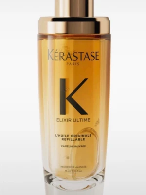 Kérastase Elixir Ultime hårolja - Lyxig hårolja från Kérastase, Elixir Ultime L'Huile Originale med kameliaolja. Flaskan är genomskinlig med guldigt lock och etikett, och oljan har en gyllene färg. Kommer i elegant förpackning med gulddetaljer. Perfekt för att ge glans och näring till håret.