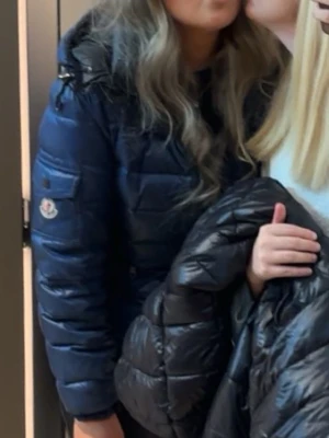 Mörkblå dunjacka från Moncler - Säljer en mörkblå dunjacka från Moncler med glansig finish och klassisk quiltad design. Jackan har hög krage, diskret Moncler-logga på ärmen och dragkedja framtill. Perfekt för kalla vinterdagar och riktigt snygg till streetwear. Finns några skador på jackan men annars superfin!!❤️