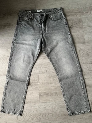 Grå loose fit jeans Jack & Jones - Säljer ett par grå loose fit jeans från Jack & Jones, modell Chris. Jeansen har klassisk femficksdesign, knappgylf och är tillverkade i slitstark bomull. Perfekta för en avslappnad och trendig stil.