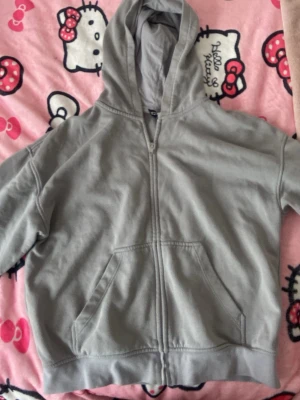 Grå zip hoodie från QED London - En enkel och clean grå zip hoodie från QED London. Hoodien har dragkedja framtill, stor känguruficka och en rejäl huva. Perfekt för chill dagar eller när du vill ha en avslappnad look. Tillverkad i mjukt bomullsmaterial. Finns en liten vit fläck vid armen som visas i bild 