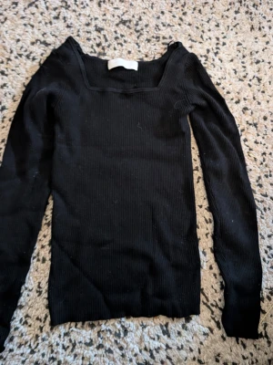 Svart ribbad topp från SAMSA stl s - Svart långärmad topp från SAMSA Collection med ribbad struktur och fyrkantig ringning. Toppen har en tight passform och är perfekt för att styla med både jeans och kjol. Tillverkad i mjukt material som sitter skönt mot kroppen.