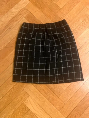 Svart rutig kortkjol - Snygg svart kortkjol med vitt rutmönster. Kjolen har en klassisk rak passform och är perfekt för att skapa en stilren look. Passar till både sneakers och boots för en trendig outfit.Skriv gärna för mått! 💕