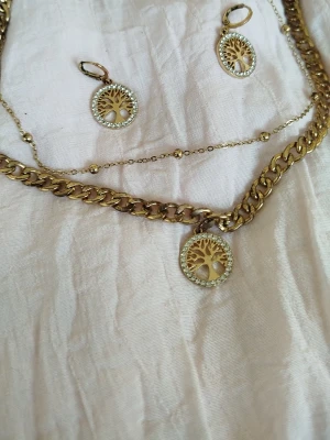 Guldhalsband med livets träd-hänge - Snyggt guldhalsband med ett runt hänge i form av livets träd, dekorerat med gnistrande stenar runt kanten. Kedjan är grov och har en trendig look. Hänget ger halsbandet en unik och personlig touch. Perfekt för dig som gillar detaljer och symbolik.250kr skickar med postnord om vid intresse 🌸🌸🌸