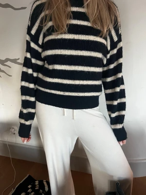 Randig stickad tröja i marinblått - Säljer en stickad tröja med breda marinblå och vita ränder. Tröjan har en avslappnad passform, långa ärmar och ribbade muddar vid ärmslut och nederkant. Perfekt för dig som gillar klassisk och enkel stil.