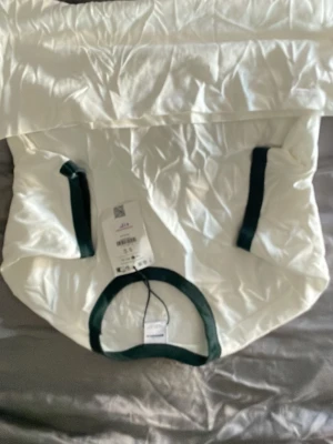 Vit t-shirt med gröna detaljer Bershka - Vit t-shirt från Bershka med gröna kontrastdetaljer vid halsringning och ärmslut. Klassisk rund hals och korta ärmar. Tillverkad i mjuk bomull som känns skön mot huden. Perfekt för en clean och enkel stil.