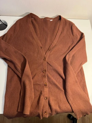 Rostbrun ribbad kofta med knappar - Snygg rostbrun kofta med ribbad struktur och v-ringning. Koftan har långa ärmar och stängs med fem matchande knappar framtill. Perfekt för lager på lager och enkel att styla till olika outfits.
