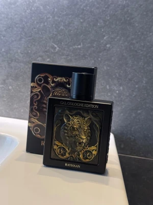 Rayhaan Cal Cologne Edition parfym - Endast testad !!Snygg parfymflaska från Rayhaan, Cal Cologne Edition. Flaskan är svart med ett detaljerat lejonhuvud i guld på framsidan och har en fyrkantig form. Kommer med matchande svart och guld förpackning. Perfekt för dig som gillar unika och lyxiga designer.