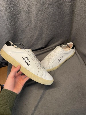 Saint Laurent skor - Snygga vita sneakers från Saint Laurent med   handskriven logga på sidan. Skorna har tecken på användning och har ett hål på sidan som blivit lagad (hålet är kvar men syns och känns knappt) (se på bild 1) nypris ligger på 7000.  Storlek 41.                 Skriv vid frågor, pris kan diskuteras🤝