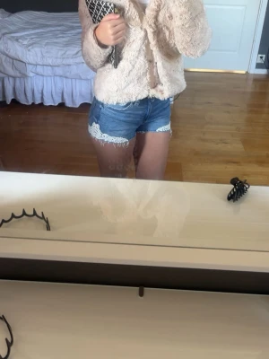 Blå jeansshorts med spetsdetaljer - Säljer ett par blå jeansshorts med vita spetsdetaljer längs bensluten. Shortsen har klassisk femficksdesign och är midwaist. Perfekta för sommaren och ger en söt och trendig look.