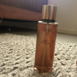 Victoria's Secret Bare Vanilla mist - Victoria's Secret Bare Vanilla är en body mist i en elegant, genomskinlig plastflaska med guldigt lock. Doften har en varm och söt vaniljton som känns lyxig och ungdomlig. Flaskan rymmer 250 ml och har en stilren design med guldiga detaljer.