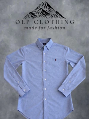 Blå slim fit skjorta från Ralph Lauren - Klassisk ljusblå skjorta från Ralph Lauren i slim fit-modell. Skjortan har långa ärmar, knappar framtill och button-down krage. Tillverkad i bomull och pryds av den ikoniska broderade loggan på bröstet. Perfekt för en clean och stilren look. Nästan aldrig använd, i perfekt skick. #7