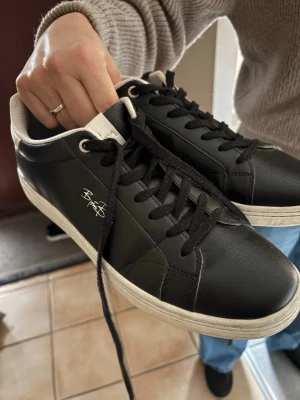 Svarta sneakers från Björn Borg - Stilrena svarta sneakers från Björn Borg med vita detaljer och svart snörning. Skorna har en låg profil och är tillverkade i slätt konstläder med vit sula. Perfekta för en clean och klassisk look.
