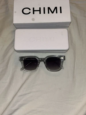 Svarta solglasögon från CHIMI - Snygga svarta solglasögon från CHIMI med klassisk rektangulär form. Bågarna är i blank svart plast med CHIMI-logga på sidan och har en stilren, modern look. Perfekta för dig som vill ha en clean och trendig accessoar till sommaren.