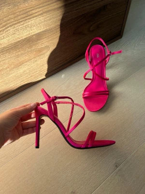 Rosa klackar från Zara - Säljer ett par trendiga rosa sandaler från Zara med smala remmar och hög klack. Sandalerna har öppen tå och justerbar ankelrem för perfekt passform. Tillverkade i syntetmaterial med en stilren och modern design.