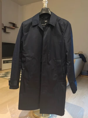 Rock/  trenchcoat mörkblå - Stilren mörkblå trenchcoat/ rock från H&M med klassisk krage och dolda knappar framtill. Jackan har raka fickor på sidorna och justerbara ärmslut med knapp. Nypris 799, knappt använd.