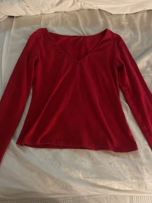 Röd långärmad v-ringad topp - Snygg röd topp med v-ringning och långa ärmar. Perfekt att styla med jeans eller kjol för en trendig look. Materialet känns mjukt och stretchigt, vilket gör den bekväm att bära hela dagen.