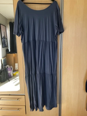 Mellanblå långklänning med kort ärm/Odd Molly - En enkel och stilren mellanblå långklänning med korta ärmar och rund halsringning. Klänningen har en lös passform och är sydd i flera våder för en avslappnad look. Perfekt för dig som gillar minimalistisk stil.