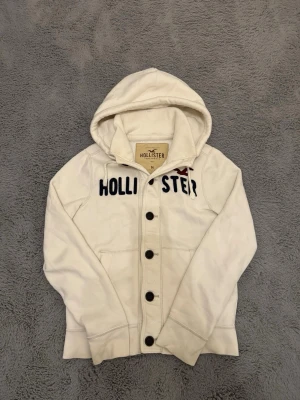 Vit vintage cardigan från Hollister med knappar - Säljer en snygg vintage cardigan från hollister i storlek M. Tröjan är väldigt sällsynt och eftertraktad pga att den inte tillverkas längre. Tröjan är dessutom i sjunket bra skick. Priset går absolut att diskuteras så kom gärna med bud👍.