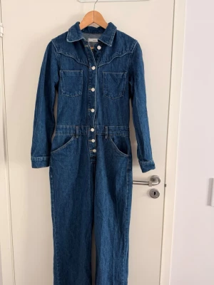 Mörkblå denim byxdress från Mango - Snygg blå denim jumpsuit från Mango i storlek S med en tight passform. Klassisk krage och western-inspirerad söm. Perfekt för dig som gillar en avslappnad men trendig look. Knappt använd och i fint skick.