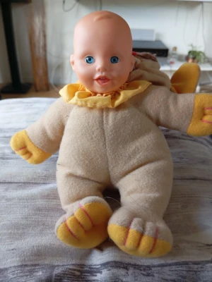 Docka i lejonpyjamas mjukisdjur - Söt docka med mjuk kropp klädd i beige och gul lejonpyjamas. Pyjamasen har öron, svans och tassar med rosa detaljer. Huvudet är i plast och resten av dockan är i mjukt tygmaterial. Perfekt som gosedjur eller leksak.