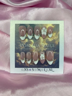 DewKiss (S);Medium Almond - Handgjorda press-on naglar i en medium lång almondform. Designen har en nude bas, vita franska tippar, silverglittrande linjer med kristaller och söta vita-blommor. Perfekt för dig som vill ha en elegant och unik look. S: 15 mm, 11,5 mm, 12 mm, 11 mm, 9 mm 