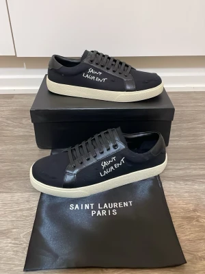 Saint Laurent sneakers - Svarta sneakers från Saint Laurent med vit sula och handskriven logga på sidan. Skorna har snörning, rund tå och är tillverkade i en mix av skinn och textil. Klassisk låg modell som ger en clean och stilren look.