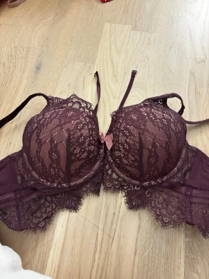Vinröd spets-bh från Hunkemöller - Snygg vinröd bh från Hunkemöller med vadderade kupor och vacker spetsdetalj över hela bh:n. Dekorativ rosett framtill och justerbara axelband. Materialet är en mix av spets och mesh som ger en lyxig känsla. Aldrig använd bara tvättad. 