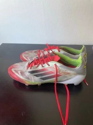 F50 - Säljer ett par Adidas fotbollsskor med röd och vit ovandel, svarta detaljer och gula inslag vid hälen. Skorna har röda snören och en låg profil med dobbar för spel på gräs. Snygg design med klassiska Adidas-ränder på sidan och grön insida. Tar även emot seriösa byten!!!