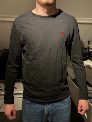 Svart långärmad tröja från Ralph Lauren - Snygg svart långärmad tröja från Ralph Lauren med klassisk röd logga broderad på bröstet. Tillverkad i mjuk bomull som känns skön mot huden. Enkel och stilren design med rund halsringning, perfekt till jeans eller andra favoritplagg.