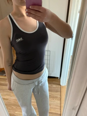 Svart linnetopp  - Säljer en svart linnetopp med vita kontrastkanter och logga på bröstet. Toppen är tight och ärmlös med sportig look, perfekt för dig som gillar enkel men snygg stil. Vet ej om den är äkta. Kolla alla bilder 