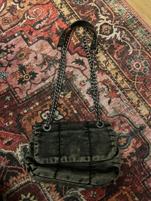 Svart quiltad axelremsväska med kedja - Snygg väska i jeans material. Använd fåtal gånger. Längden går att justera.
