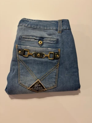 Roy Roger’s Made in Italy jeans 26/ IT40 ljus tvätt med ankelzip  - Snygga ljusblå jeans från Roy Rogers med unika detaljer som dekorativa sömmar och metallspänne på bakfickan. Klassisk femficksmodell med guldfärgade nitar och logotyp på fickan. Tillverkade i mjukt denimtyg som ger en avslappnad look. W26 och ungefär EU36/IT40